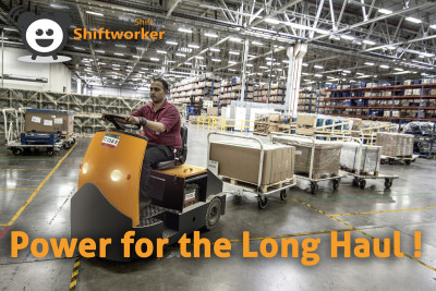 Shiftworker warehouse worker driving a factory tow tractor moving pallets, demonstrating energy and focus on the job.
